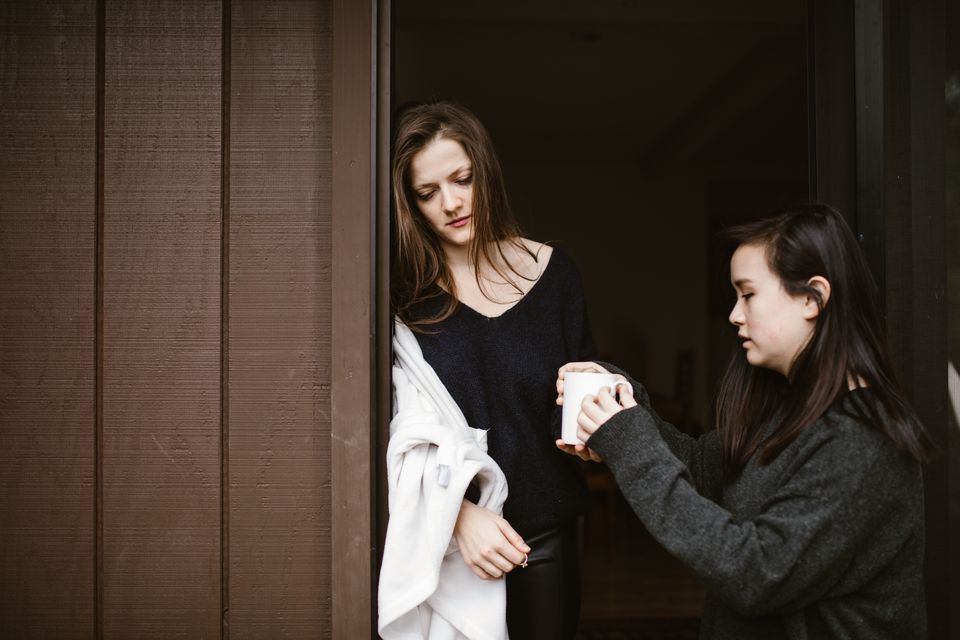 A woman handing a comforting cup of tea to a friend at home