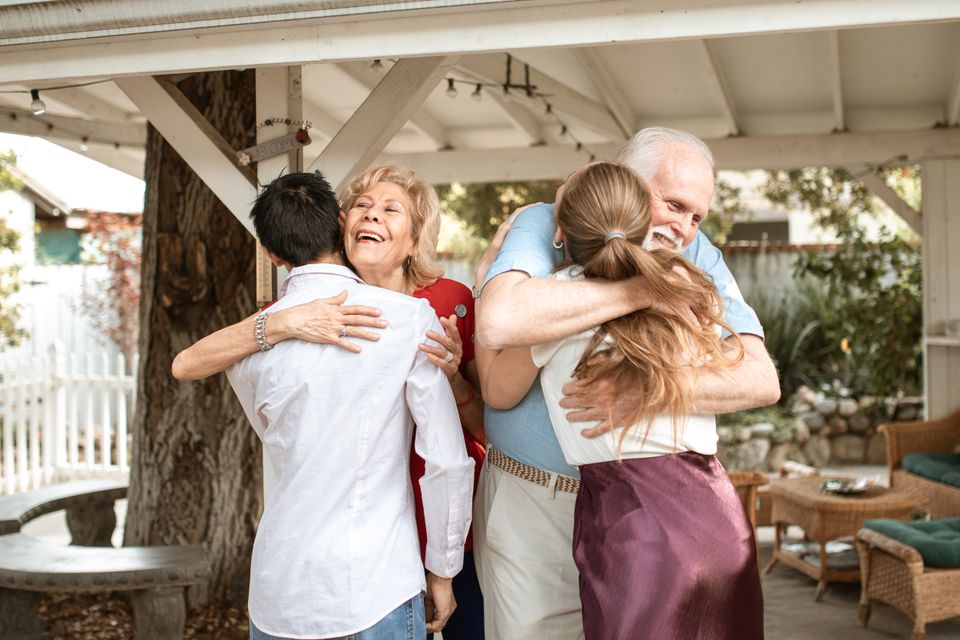 A multigenerational family greeting one another with hugs outdoors