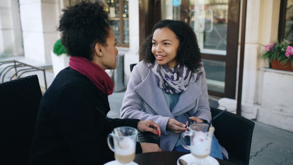 Two women in warm conversation over coffee at an outdoor cafe