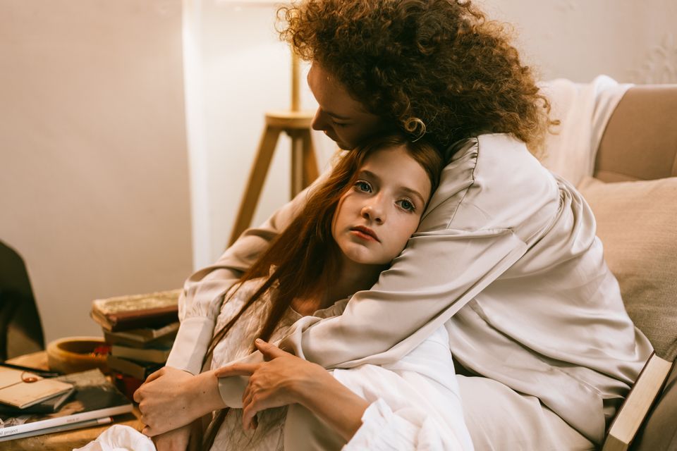 A woman embracing a teenage girl in a warm living room